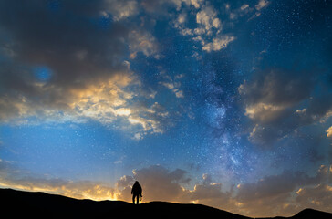 Fototapeta premium Silhouette of a person in the sunset and stars. Photographer silhouette stands on the hill with camera.