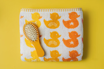Baby towel with cute ducks and hairbrush on yellow background. - obrazy, fototapety, plakaty