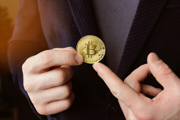 Close up of a man dressed in suit holding golden bitcoin on his palm and pointing finger isolated over gray background