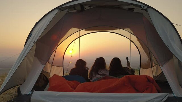 girl friend group Asians laying in tents during camping are waking up to watch the sun rise and shoot video from their action cams to show off to their friends in social media, the concept of adventur