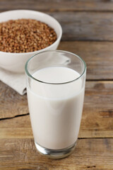 Dairy free buckwheat milk in a glass and seeds in a bowl on wooden background