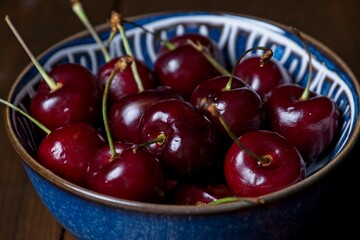 Close-up of red cherries in blue bowl on dark wooden surface