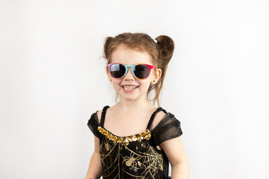 A little playful girl with two ponytails and a black and gold dress. Studio photo on a white background of a child in sunglasses