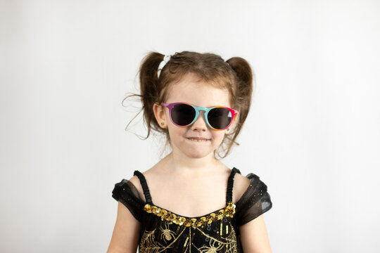 A little playful girl with two ponytails and a black and gold dress. Studio photo on a white background of a child in sunglasses