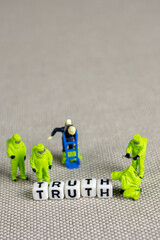 the team of miniature figurines of special doctor forces seting up a word truth made of white cubes on grey background
