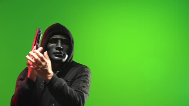 Masked man wearing a black hooded sweater carrying and pointing a gun and taunting - shot on green screen