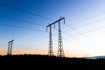 Fototapeta premium Power lines against the background of a evening sky above black silhouette forest. Air acrossing and perspective of electrical wires of power transmission lines. Corridor of power lines