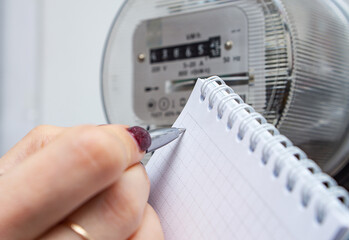 Ballpoint pen in woman's hand for writing electricity meter readings. Distribution of electricity...