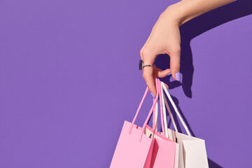 Womans hand holding paper shopping bags on purple background. Shopping sale delivery concept