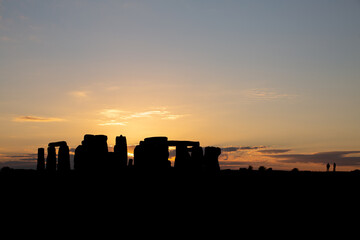 Stonehenge at sunrise with 2 people standing next to the prehistorical monument