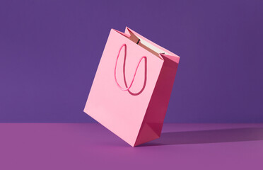Pink flying paper shopping bag on purple background. Shopping sale delivery concept