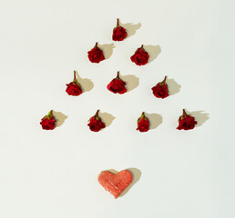 A geometrical floral composition made of fresh rose buds in a shape of triangle with a heart underneath on white background. Minimalist concept of love. Anniversary or Valentine’s pattern. Copy space.