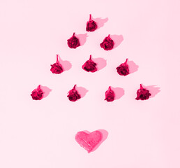 A geometrical floral composition made of fresh rose buds in a shape of a triangle with a heart underneath on pink background. Minimalist concept of love. Anniversary or Valentine’s pattern. Copy space