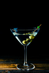 Elegant dry martini glass with sprinkled olives on black background with copy space. Vertical orientation.