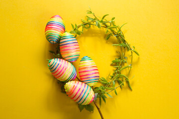 A wreath of young spring leaves on branches with colorful Easter eggs. Nest with eggs on a yellow background.