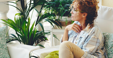 One woman sitting at home in the garden with green plants around and looking. Thoughtful female...