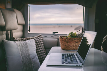 Fototapeta Remote onilne work and smart working travel concept with laptop computer inside a van camper interior with beach view. Freedom from office modern lifestyle for alternative life and people obraz
