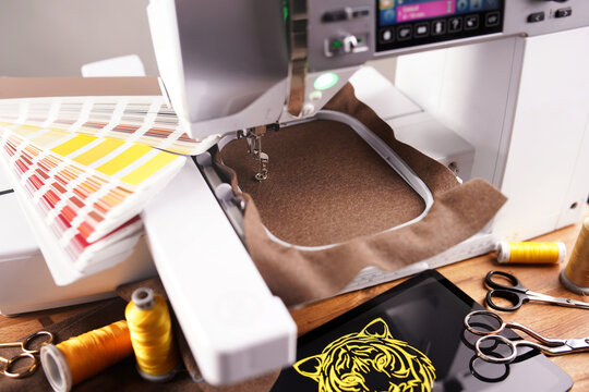 workplace for golden tiger head embroidery with embroidery machine, tools, yarn samples, color fan and tablet computer. color decision. work preparation. brown merino wool fabric in embroidery hoop.