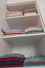 Obraz na płótnie Canvas Pastel clothes folded on shelves in wardrobe