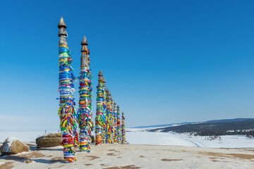 A row of high ritual cult pillars of the Buryats, tied with multi-colored ribbons, on a clear winter day. Sacred Cape Burkhan, Shamanka rock, lake Baikal, Siberia, Russia. Copy space - 480615968