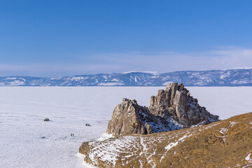 Sacred Shamanka Mountain on Olkhon Island in winter. View of the frozen Lake Baikal on a sunny day. View from above. Below, tourists walk on the ice