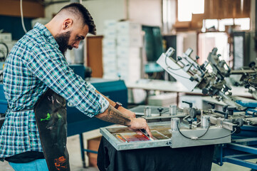 Male worker pressing ink on frame while using the printing machine in a workshop