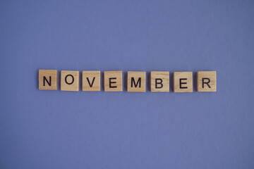 The name of the month of November is written on wooden cubes isolated. Very Peri Color of the Year 2022 background, copy space. Top view of wooden blocks with letters. Step by step, step 11.
