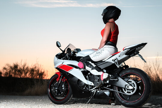 young biker woman with black safety helmet sitting on her motorcycle resting contemplating the sunset
