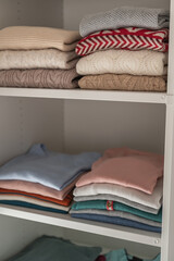 Pastel clothes folded on shelves in wardrobe