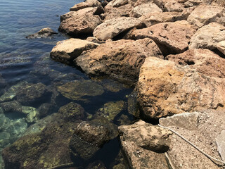 Turquoise sea stone beach, breaking waves in bright sunlight. Colorful bright sea background. The concept of summer, vacation, travel. The purest clear sea water, large stones on the beach close-up