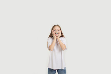 Portrait of an admiringly smiling girl holding hands near her face. standing on a white background.