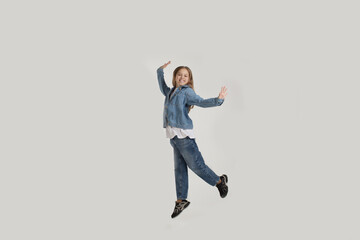 Fototapeta na wymiar a young girl in jeans jumps with happiness on a white background with a copy of the space