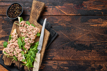 Canned Tuna Toasts or Sandwich with lettuce and arugula. Dark Wooden background. Top view. Copy space