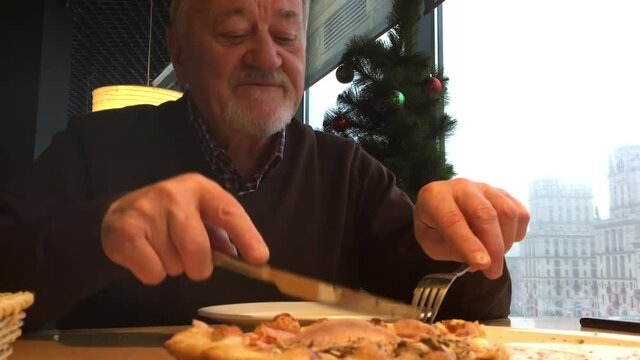 Happy senior man eating pizza in a bar, talking and smiling. Elderly resting in a Christmas setting. The concept of active longevity, successful old age