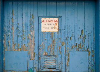 An old weather beaten wooden door that has been painted blue and has a no parking sign on it.
