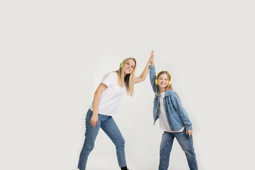 A beautiful young woman with her cute little daughter dancing in yellow headphones on a white isolated background.