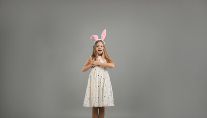 a beautiful young girl with rabbit ears looks admiringly into the camera holds her hands on her chest on a gray isolated background