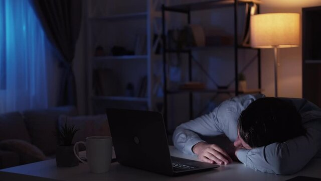 Home movie. Sleeping man. Digital technology. Tired guy sitting desk laying on hands while on laptop showing video light shadow room interior.