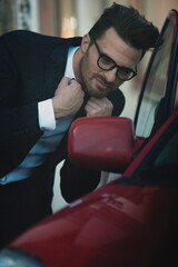 Handsome gentleman in suit and with bow tie,shirt, with glasses, looking at car mirror
