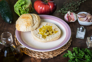 Bread roll with oil and all the ingredients to make a vegetarian sandwich (lettuce, tomato, cucumber and garlic).