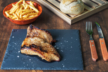 Grilled pork (secret) served on a stone plate and accompanied by chips and bread on a wooden background.