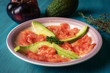 Plate to snack with avocado and tomato accompanied by oil and salt flakes. Close-up.