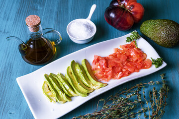 Plate to snack with avocado and tomato accompanied by oil and salt flakes.