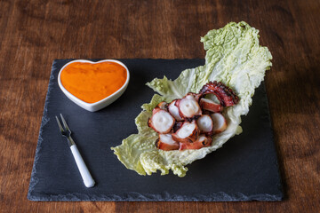 Dry octopus leg, on a bed of cabbage on a stone plate, accompanied by mojo picon sauce.