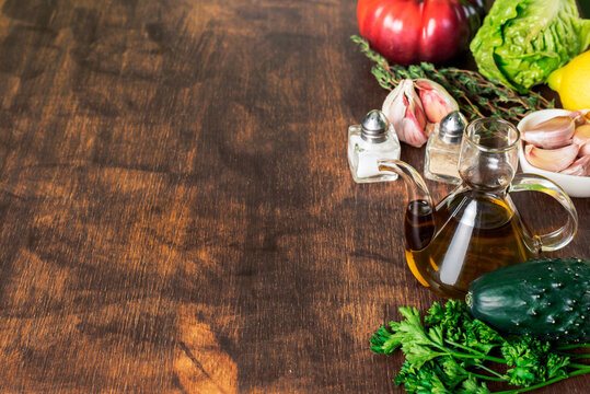 Wooden background in worn brown color, on one side with vegetables, oil, salt and pepper.