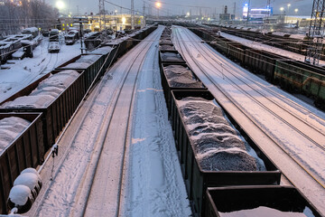 A freight train carries a cargo of coal in bulk containers covered with snow in winter at the station. Top view from the bridge