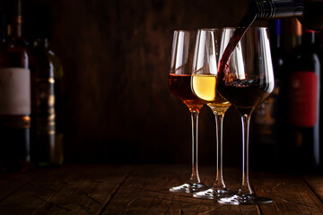 Red, white and rose wine in glasses on wooden background and collection of wine bottles, copy space