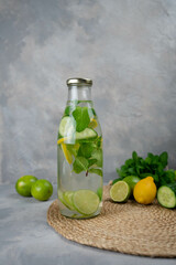 Detox Sassy water with lemon, cucumber, mint. A bottle of clean, cool and fresh drink stands on a gray concrete background with ingredients on board. Strengthening immunity, diet.