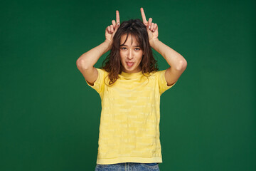 Funny young girl make horns by fingers, making faces, showing tongue, having fun, grimacing,...