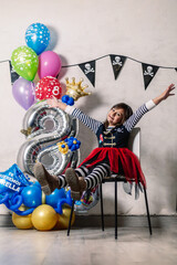 little girl dressed as a pirate, hands up, sitting on a chair, with number eight celebration balloons